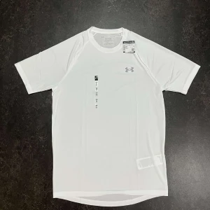 Vit Under Armour Tech t-shirt - Snygg vit t-shirt från Under Armour med klassisk logga på bröstet. Tillverkad i lätt och snabbtorkande polyester, perfekt för träning. Modellen har korta ärmar och en loose fit som ger skön rörelsefrihet. Enkel och stilren design som funkar till alla sportiga outfits.