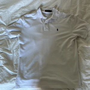 Vit pikétröja från Polo Ralph Lauren - Klassisk vit pikétröja från Polo Ralph Lauren i bomull. Tröjan har korta ärmar, krage med knappar och den ikoniska broderade loggan på bröstet. Perfekt för en clean och stilren look. Precis som ny, Är för stor för mig som har Medium så tror att den skulle passa L också. Nypris: 1595