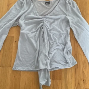 Ljusblå långärmad omlottopp - Supersöt ljusgrå omlottopp från Gina Tricot med v-ringning och snygg snörning framtill. Topp i mjukt bomullsmaterial, långärmad och croppad passform. Perfekt till jeans eller kjol för en chill look. liten månar fläck som syns på sista bilden 