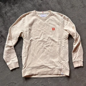 Beige sweatshirt från Les Deux - Snygg beige sweatshirt från Les Deux med rund halsringning och diskret logga på bröstet. Tröjan har långa ärmar, ribbade muddar och är gjord i mjuk bomull. Perfekt för en chill och stilren look. Stl L