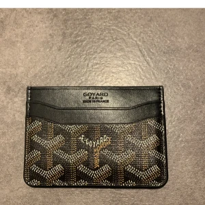 Goy4rd svart plånbok med mönster - Säljer en stilren svart plånbok från goy4rd  med deras ikoniska grafiska mönster i beige, brunt och vitt. Plånboken har flera kortfack och är tillverkad i exklusivt skinn. Perfekt för dig som vill ha något lyxigt och klassiskt i fickan.