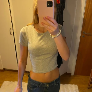 Grå croppad t-shirt - Säljer en enkel och stilren grå croppad t-shirt med rund hals och korta ärmar. Perfekt till jeans eller kjol för en avslappnad look. T-shirten är i mjukt bomullsmaterial och har en tight passform 