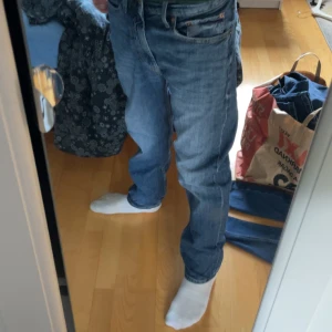 Blå jeans från Dressmann, storlek 29/30 - Snygga blå jeans från Dressmann i klassisk femficksmodell. Jeansen har en rak passform med normal midja och är tillverkade i slitstarkt denimtyg. Färgen är mellanblå med lätt tvättade detaljer och kontrastsömmar. Perfekta för en chill och stilren look.
