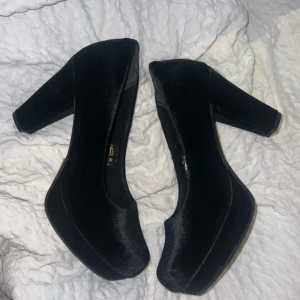 Svarta pumps i sammet från Vox - Säljer ett par svarta pumps från Vox med chunky klack och rund tå. Skorna är gjorda i mjuk sammet som ger en lyxig känsla och har en plattformsdesign för extra höjd. Perfekta för dig som vill sticka ut med stil och komfort.