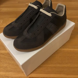 Svarta Maison Margiela sneakers - Maison Margiela sneakers i svart med beige insida och snörning. Snygg kombination av mocka och skinn på ovandelen, samt en klassisk gummisula i brunt. Storlek 43 och nästan perfekt skick, skriv vid funderingar eller om du vill se flera bilder😆😆