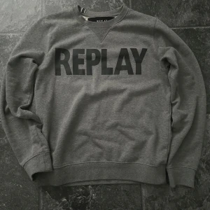 Grå sweatshirt från Replay i M - Snygg grå sweatshirt från Replay med stor svart logga över bröstet. Tröjan har rund hals, ribbade muddar och är tillverkad i mjuk bomullsmix som är skön mot huden. Perfekt för chill dagar och enkel att matcha med jeans eller joggers. Priset kan diskuteras vid snabb affär.