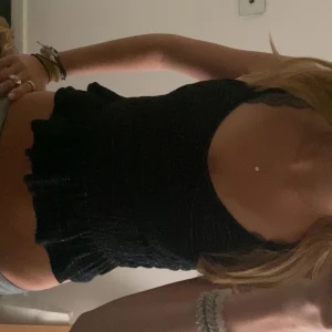 Svart glittrig croppad linnetopp - Supersöt svart v-ringad croppad linnetopp med tunna axelband och glittriga silvertrådar. Toppen har smockad struktur vilket gör den ganska stretchig och en volangkant nedtill som ger en extra touch. Perfekt för dig som vill sticka ut lite extra med en enkel men snygg topp! Toppen är i superfint skick! den är ganska kort! Det står inte storlek på den men skulle säga att det är xs! 