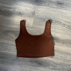 Brun croppad linnetopp - Snygg brun croppad linnetopp med breda axelband och rundad halsringning. Perfekt att styla med höga jeans eller kjol för en trendig look. Enkel och stilren design som passar till många outfits.