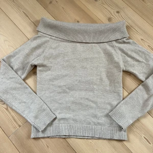 Beige offshoulder stickad tröja Gina Tricot - Superfin beige stickad tröja från Gina Tricot med bred ribbad offshoulder-krage. Långärmad modell med ribbade muddar och nederkant. Perfekt för dig som gillar en stilren och trendig look.