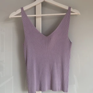 Ljuslila ribbad linnetopp från JDY - Superfin ljuslila ribbad linnetopp från JDY med v-ringning och smala axelband. Toppen är ärmlös och har en slim passform som sitter snyggt på kroppen. Perfekt att styla med jeans eller kjol för en fräsch look.