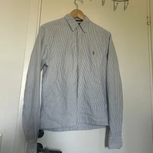 Randig skjorta från Polo Ralph Lauren - Säljer en fet skjorta från polo Ralph lauren, designen är randig med blått och vitt. Skön sommarskjorta då den är tillverkat i mjuk bomull, perfekt för en stilren minimalistisk look till våren och sommaren, kragen har lite slit (bild 5) men inget som syns när man har på den därav priset, men annars är de inga defekter på den. Om du vill ha fler bilder är de bara att fråga och priset är alltid diskuterbart !! Passa på när de är fri frakt !!