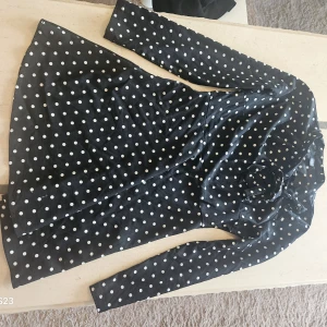 Svart prickig klänning från SHEIN - Supersöt svart klänning med vita prickar från SHEIN. Klänningen har lång ärm, markerad midja och lätt utställd kjol. Perfekt för dig som gillar retrovibbar och vill sticka ut lite extra. Materialet är mjukt och följsamt.