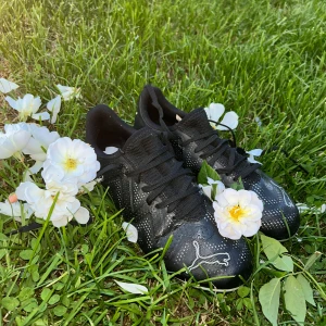Svarta fotbollsskor från Puma - Svarta fotbollsskor från Puma med vita detaljer och logga framtill. Skorna har snörning, låg profil och är tillverkade i syntetmaterial med små vita prickar över hela ovandelen. Perfekta för dig som vill ha stilrena och sportiga skor på planen.