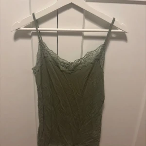 Olivgrön linnetopp med spets Tezenis - Supersöt olivgrön linnetopp från Tezenis med tunna axelband och vacker spetsdetalj längs urringningen. Perfekt att styla lager på lager eller till jeans. Mjuk och skön känsla, passar dig som gillar en enkel men ändå feminin look.