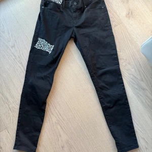 Svarta skinny jeans med leopardpatch - Svarta skinny jeans med coola leopardmönstrade patchar vid fickan och på låret. Jeansen har klassisk femficksdesign och smal passform. Perfekta för dig som vill sticka ut med en unik detalj i outfiten. 