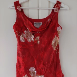 Röd blommig topp Papell Boutique - Supersnygg röd topp från Papell Boutique med blommigt mönster och draperad urringning. Ärmlös modell i tunn, lätt tygblandning av rayon och silke med polyesterfoder. Perfekt för dig som vill sticka ut med en färgstark look.