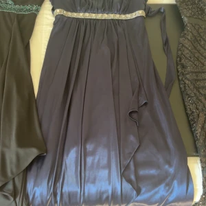 Långklänning i mörkblå satin med pärldetalj - Elegant långklänning i mörkblå satin med glansig finish och vackert fall. Klänningen använd fåtal ggr därav mycket bra skick. Köpt i usa , säljer för 738 kr . Köparen står för frakt. 