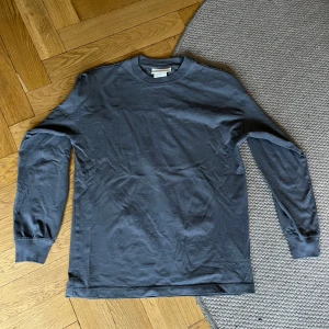 Mörkgrå långärmad tröja från H&M - Säljer en mörkgrå långärmad tröja från H&M i storlek XS. Tröjan har rund halsringning, ribbade muddar vid ärmslut och är gjord i mjuk bomull. Perfekt för lager-på-lager och enkel att matcha med allt.