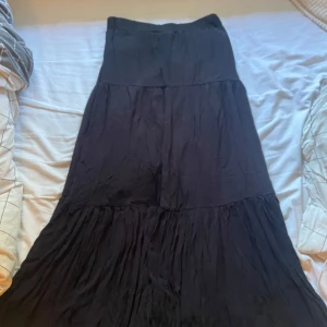 Svart långkjol med volang - Säljer en svart långkjol med volangdetaljer. Kjolen har en flowy och luftig känsla, perfekt för dig som gillar en avslappnad men ändå stilren look. Passar till sneakers eller boots och är enkel att matcha med olika toppar.