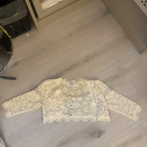 Vit spets bolerotopp från Rosemunde - Superfin vit bolerotopp från Rosemunde i genombruten spets med blommigt mönster. Croppad modell med långa ärmar och vågig kant nertill. Perfekt att slänga över ett linne eller klänning för en extra touch.