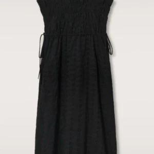 Klänningg MNG - Svart långklänning från MNG med smockad överdel och knytband i midjan. Klänningen har en elegant och enkel design, perfekt för dig som gillar stilrena plagg. Tillverkad i ett lätt material med diskret struktur.