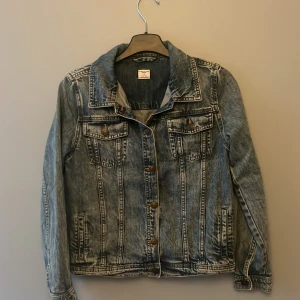 Blå jeansjacka från Polarn O. Pyret i storlek 152 - Snygg blå jeansjacka från Polarn O. Pyret i storlek 152. Klassisk modell med två bröstfickor med knappar, slitna detaljer och markerade sömmar. Perfekt för dig som gillar en avslappnad och cool stil. Jackan har långa ärmar och knäppning framtill.