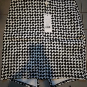 Svartvit rutig kortkjol Alexis - Snygg svartvit kortkjol från Alexis med klassiskt hundtandsmönster. Kjolen har rak passform och är perfekt för dig som gillar statement-plagg. Tjockare material som håller formen och ger en cool look.