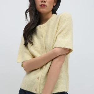 Gul stickad kofta från Gina Tricot - Superfin ljusgul stickad kofta från Gina Tricot med korta ärmar och rund hals. Koftan har ribbat material och knäpps med knappar framtill🌼