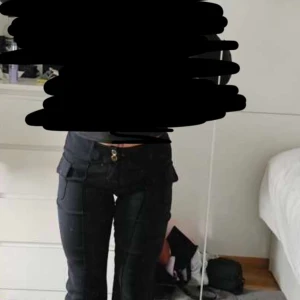 Svarta cargobyxor med bootcut - Svarta cargobyxor  med bootcut och fickor på sidorna. Byxorna har låg midja och är tillverkade i ett mjukt bomullsmaterial med lite stretch. Snygga sömdetaljer framtill och klassisk knappstängning. Original pris - 276Kr men säljs för 150kr 