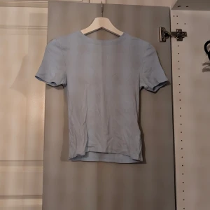 Ljusblå ribbad t-shirt - En enkel och stilren ljusblå ribbad t-shirt med korta ärmar och rund hals. Toppen har en tight passform och är perfekt att matcha med jeans eller kjol för en clean look. Mjuk och skön mot huden.