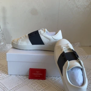 Valentino skor - Snygga Valentino Garavani Open sneakers i vitt kalvskinn med bred marinblå rem över vristen. Klassisk rund tå, vita snören och diskret logga på plösen. Perfekta för dig som gillar stilrena och exklusiva sneakers med en modern twist. Priset kan diskuteras vid snabb försäljning 