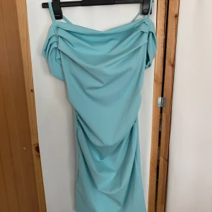 Ljusblå axelbandsklänning med drapering - Supersöt ljusblå kortklänning med smala axelband och snygg drapering framtill. Klänningen har offshoulder-detaljer och dragkedja i ryggen. Perfekt för dig som vill sticka ut med en fräsch och somrig look!