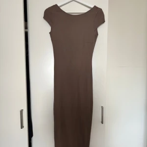 Brun långklänning från Gina Tricot - Säljer en stilren brun långklänning från Gina Tricot. Klänningen har tight passform, korta ärmar och en djup, rundad rygg. Tillverkad i mjuk bomullsmix som sitter snyggt på kroppen. Perfekt för dig som gillar minimalistisk och trendig stil.