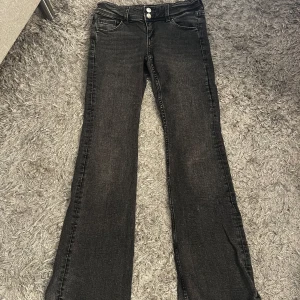 Svarta bootcut jeans med knappar - Snygga svarta jeans med bootcut passform och dubbla knappar i midjan. Klassisk femficksmodell med coola detaljer på bakfickorna. Jeansen har en lätt tvättad look och passar perfekt till sneakers eller boots.