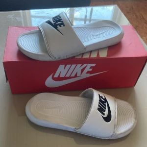 Tofflor - Jag säljer ett par vita nike tofflor köpta direkt från deras hemsida, De är i okej skick men de är även en del använda, det är en spricka mellan remmen och tofflan (se sista bild) undersidan är smutsig men de är omöjligt unvikbart på skor/tofflor (hör av dig om du vill ha bild). mycket sköna och mjuka, hör av dig vid minsta fundering.🤩(pris kan absolut gå ned vid förfrågan)
