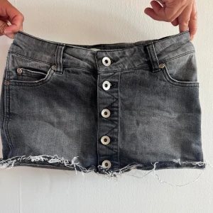Svart jeanskjol från Only med knappar - Cool svart jeanskjol från Only med slitna kanter och fem stora knappar framtill. Kjolen har klassiska jeansfickor både fram och bak samt bälteshällor. 