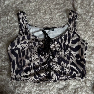 Leopardmönstrad snörad topp  - Cool croppad topp  med leopardmönster i svart och beige. Toppen har snörning framtill och breda axelband. 