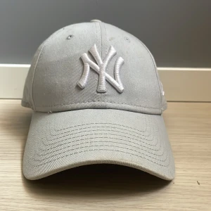 Ljusgrå New Era NY Yankees keps - Snygg ljusgrå New Era 9FORTY keps med broderad New York Yankees-logga framtill. Justerbar rem baktill med metallspänne. Klassisk böjd skärm och ventilerande hål. Perfekt för dig som vill ha en stilren och sportig look.