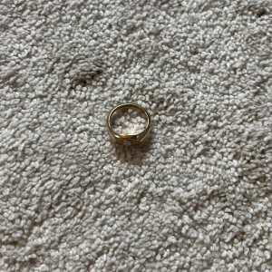 Guldfärgad ring med solmotiv - Snygg guldfärgad ring med ett solmotiv och en glittrande sten i mitten. Ringen har en chunky design och är perfekt för att ge din look lite extra edge. Passar både som statement piece eller att kombinera med andra ringar. OBS!!! KOMMER GÖRAS RENT INNAN SICKAD