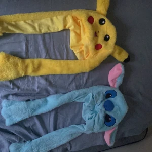 Pikachu och Stitch mössor med öron - Två mjuka och fluffiga mössor med långa öron – en gul Pikachu med broderat ansikte och svarta detaljer, samt en ljusblå Stitch med stora ögon och rosa insida på öronen. Båda har långa hängande öron som avslutas med tassar. Perfekt för dig som älskar anime och söta accessoarer.