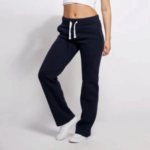 Russemerch byxor - Mörkblå russemerch mjukisbyxor med raka ben och vit snörning i midjan. Byxorna har normal passform och är tillverkade i mjukt bomullsmaterial. Perfekta för chill dagar eller när du vill vara bekväm men ändå se snygg ut.