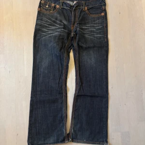True Religion jeans triple stitch super t - Fire trueys me en triple stitch super t, riktigt fina i bra skick förutom att knappen saknas fram till och lite heelbite därför det lägre priset. Använd gärna köp nu eller kontakta mig för frågor.🙏 Mått: Midja rakt över(48cm), hela längden(108cm), innerbens längd(76cm), benöppning(28cm). Priset är satt på 527kr pga att jag får prick 500kr då🙏