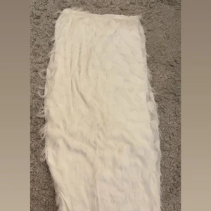 Vit långkjol med fluff från Gina Tricot - Supersnygg vit långkjol från Gina Tricot med fluffig, pälsliknande yta som ger kjolen en unik och trendig look. Perfekt för dig som vill sticka ut och älskar statement-plagg. Kjolen har en rak passform och är helfodrad för extra komfort.