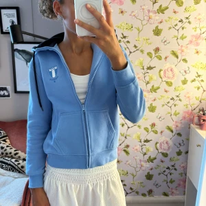 Blå Malmö FF hoodie med dragkedja - Blå hoodie från Malmö FF med klubbens logga på bröstet. Jackan har dragkedja, huva med svart insida. Perfekt för dig som vill visa vilket lag du hejar på och gillar sportig stil. Passar som en xxs