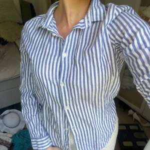 Randig blåvit skjorta i linne - Snygg skjorta med blå och vita vertikala ränder, klassisk krage och knäppning framtill. Tillverkad i svalt linne, perfekt för varmare dagar. Långärmad modell med normal passform och stilren look. Skjortan är i barnstorlek men jag skulle säga att det är som en xs.