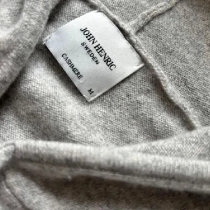 Grå kashmirhoodie från John Henric - Supermjuk och stilren ljusgrå hoodie i 100% kashmir från John Henric. Tröjan har dragkedja, snörning i huvan och två fickor framtill. Priset är inte hugget i sten. 