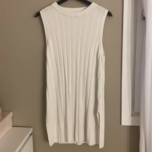 Vit ribbad ärmlös klänning H&M - Säljer en vit, ärmlös ribbad klänning från H&M i storlek M. Klänningen har en rak, enkel passform och är tillverkad i ett mjukt, stretchigt material. Perfekt för en clean och stilren look med hög halsringning och snygga vertikala ribbor.