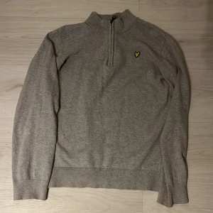 Grå half zip tröja från Lyle & Scott - Snygg grå långärmad tröja från Lyle & Scott med  gul logga på bröstet. Tröja har half zip-dragkedja framtill. Inga defekter på den, skriv vid frågor och funderingar. Priset kan alltid diskuteras😊