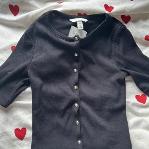 Svart ribbad topp med guldknappar H&M - Svart top med guldknappar från hm, oanvänd och med prislapp kvar