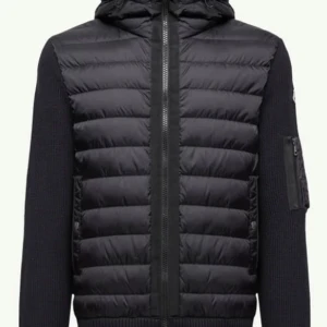 Svart Moncler pufferjacka med stickade ärmar - Svart pufferjacka från Moncler med quiltad front i dun och stickade ärmar. Jackan har huva, dragkedja framtill och en extra ficka med dragkedja på ärmen. Klassisk Moncler-logga på vänster ärm. Perfekt för dig som vill ha en clean och modern look.